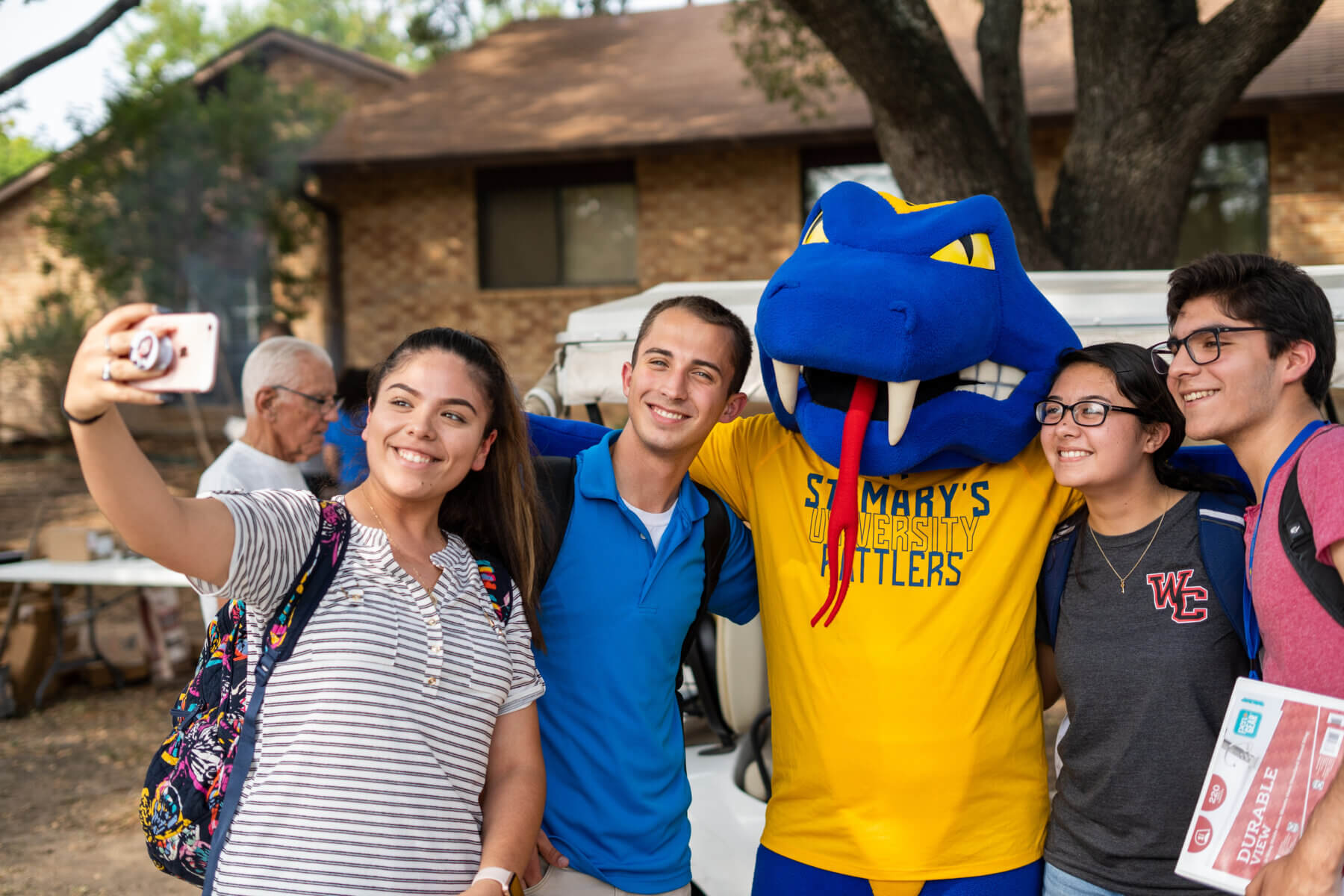 Rattler Man, the St. Mary's University mascot, poses for a selfie with a group of students.
