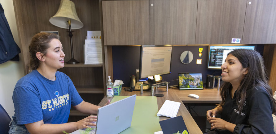 an adviser sits across a desk from a student during their financial aid appointment.