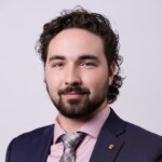 Liam Riley wearing a blue suite, pink shirt and gingham patterned tie.