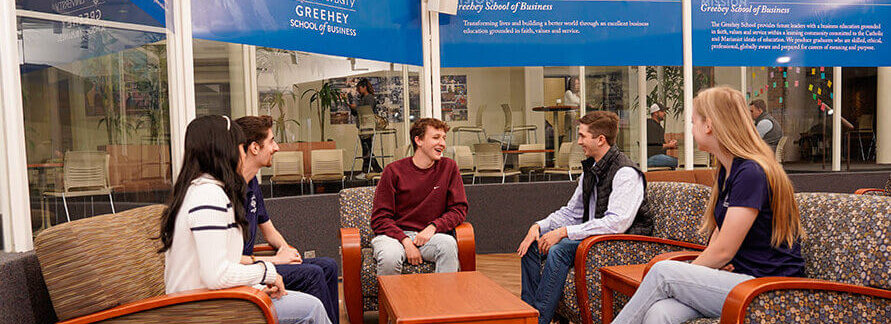 Five students sit on couches in Alkek Building surrounded by signs for Greehey School of Business