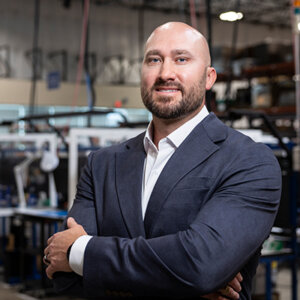 Jason Stover is photographed in a blue suit and white shirt in the warehouse of Infinite Electronics.