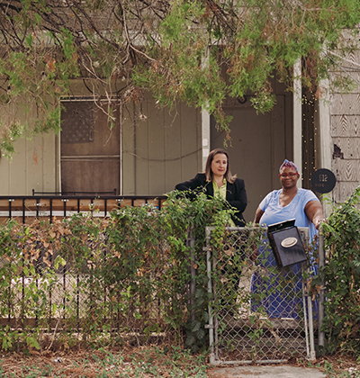 Law professor stands with resident in front of her home.