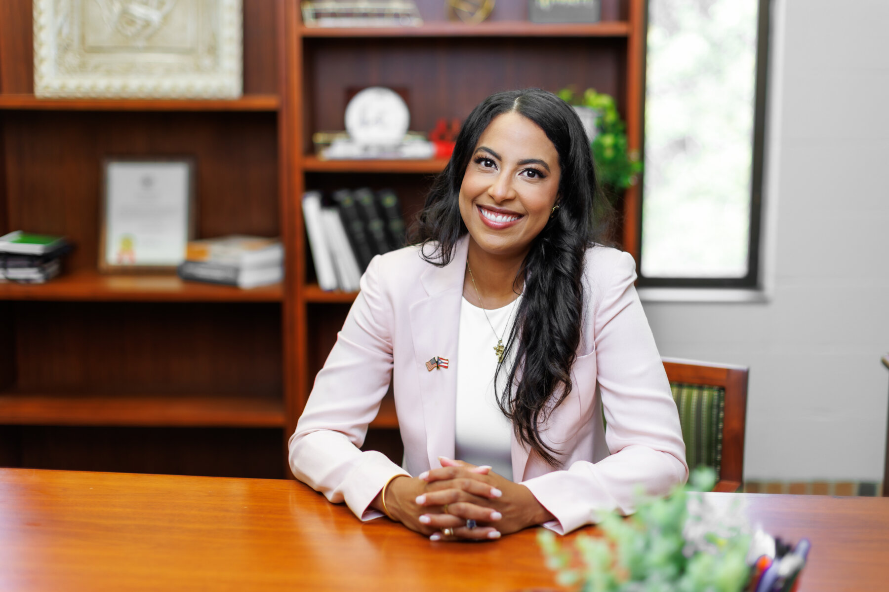 Sigrid Vendrell-Polanco is wearing a pink jacket and white blouse and is seated at her office desk.