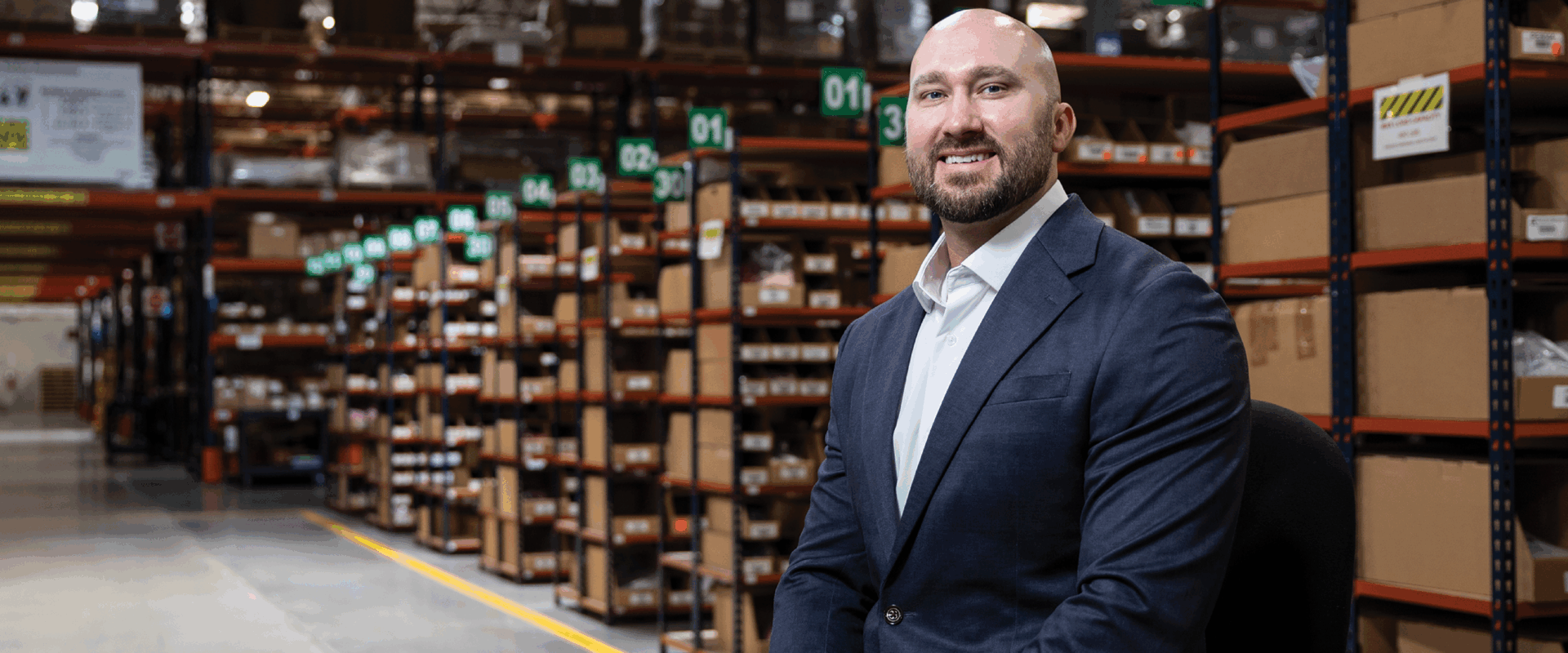 Jason Stover is photographed in a blue suit and white shirt in the warehouse of Infinite Electronics.