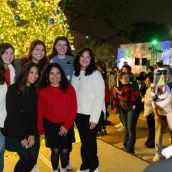 Young women pose for a photo in front of the tree at Christmas Tree Lighting 2024..