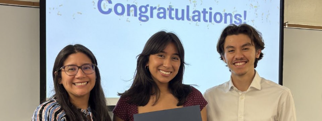 Three students holding a certificate in front of a projector with the projection saying "Congratulations!".