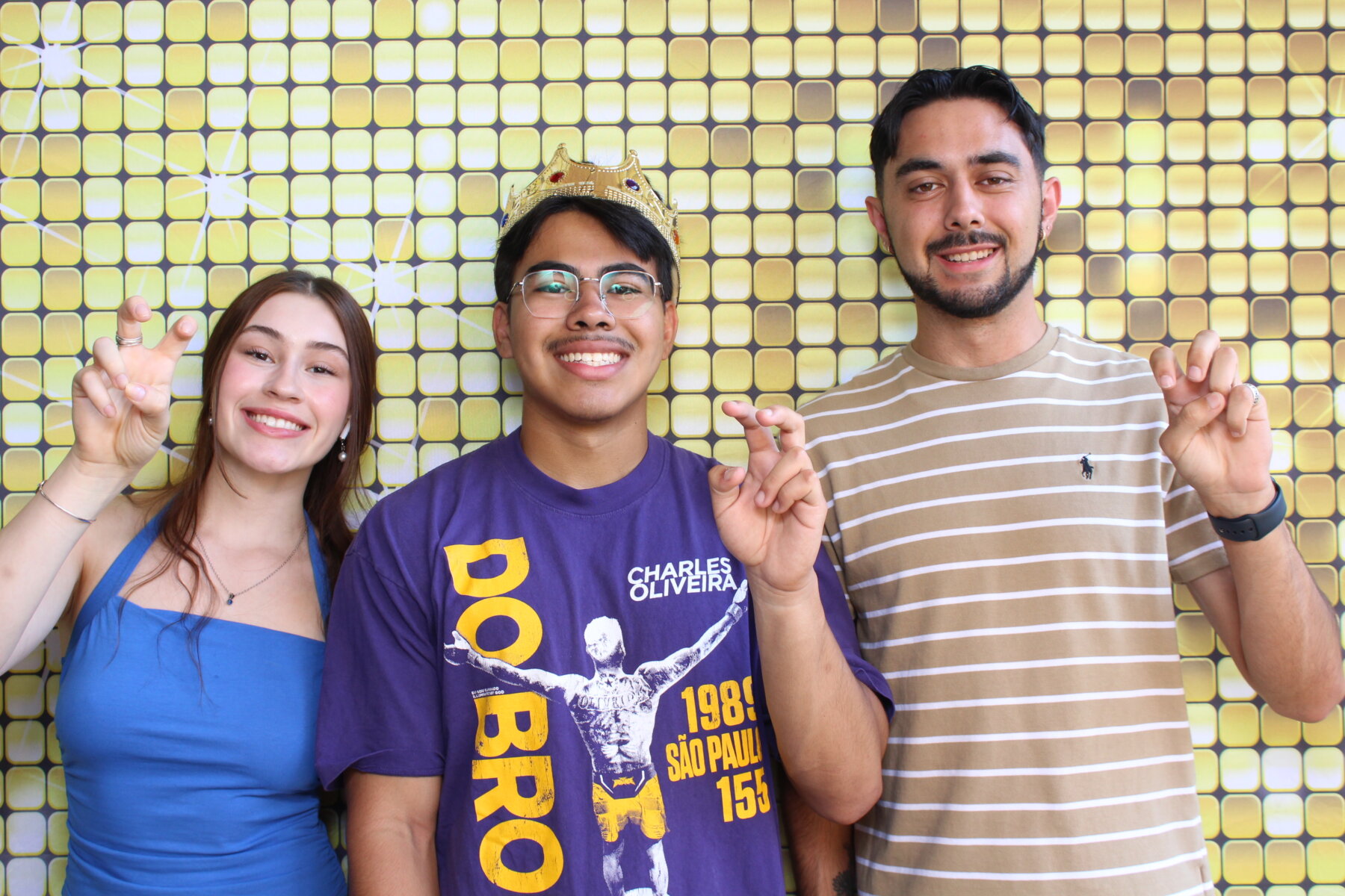 Student making the St. Mary's University hand gesture "Fangs Out" in front of a gold wall.