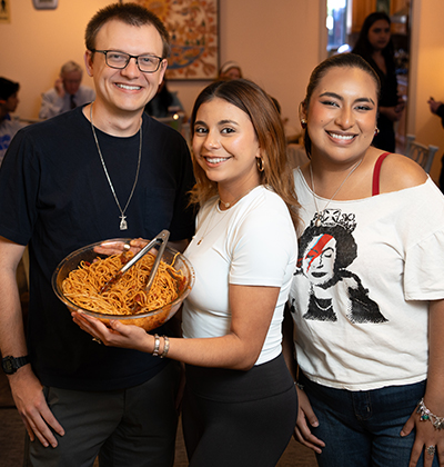 Marianist Novice Paul Pruski and St. Mary's University students Viana Galindo and Cristina Duque share in the spaghetti at a Casa Tuesday dinner in April 2025.