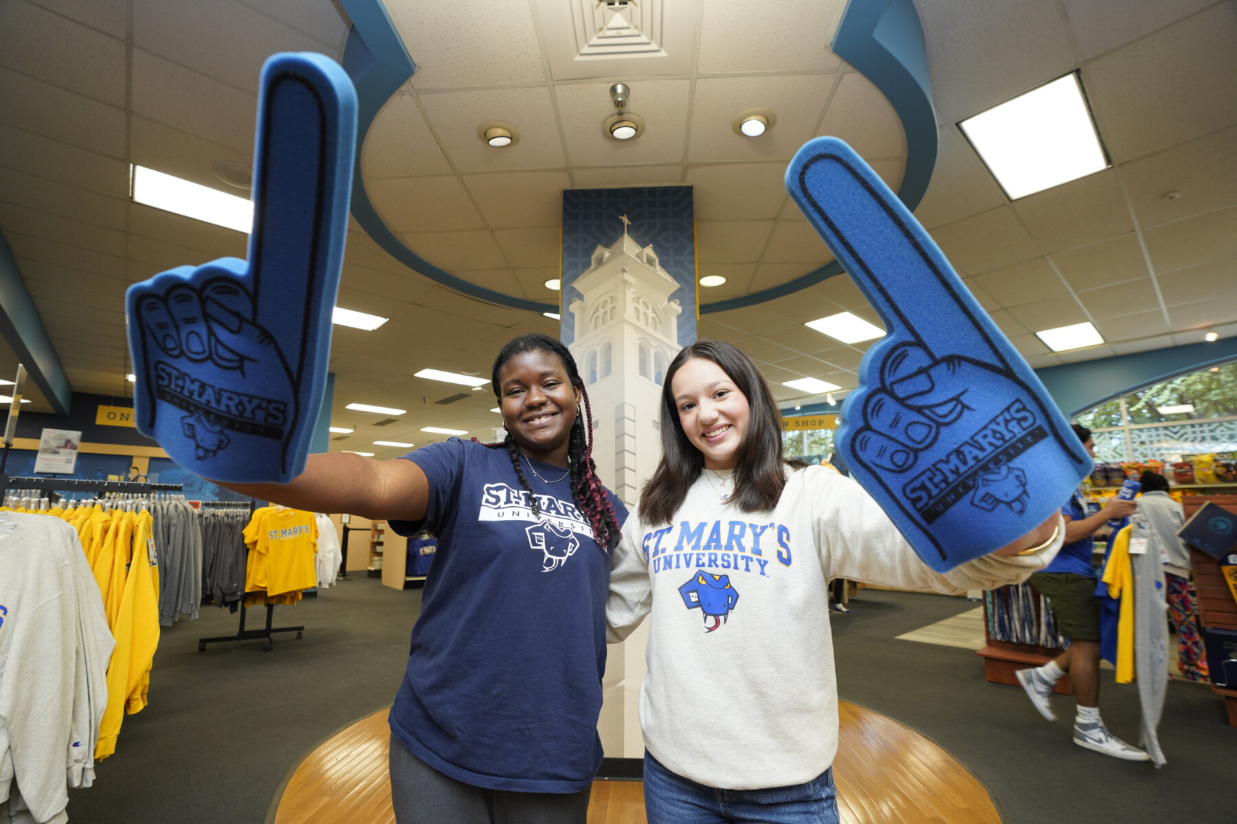 Two students holding blue St. Mary's foam fingers smile at the camera in the University's bookstore.