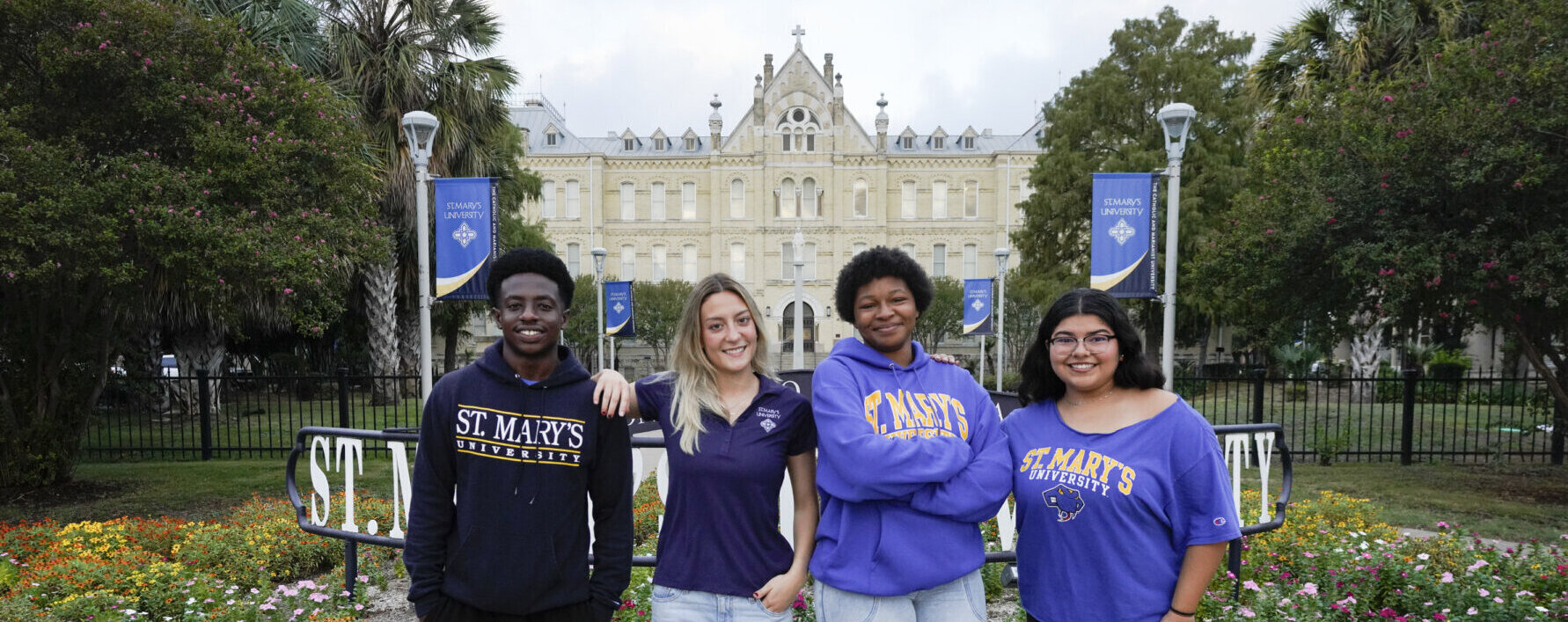 A group of students stand outside by the St. Mary's University sign in front of St. Louis Hall.