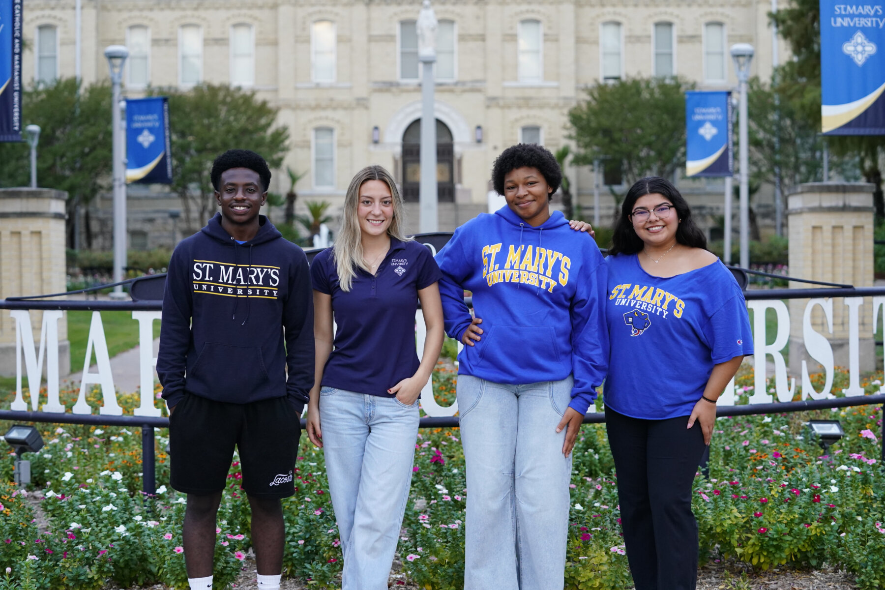 A group of students stand outside by the St. Mary's University sign in front of St. Louis Hall.