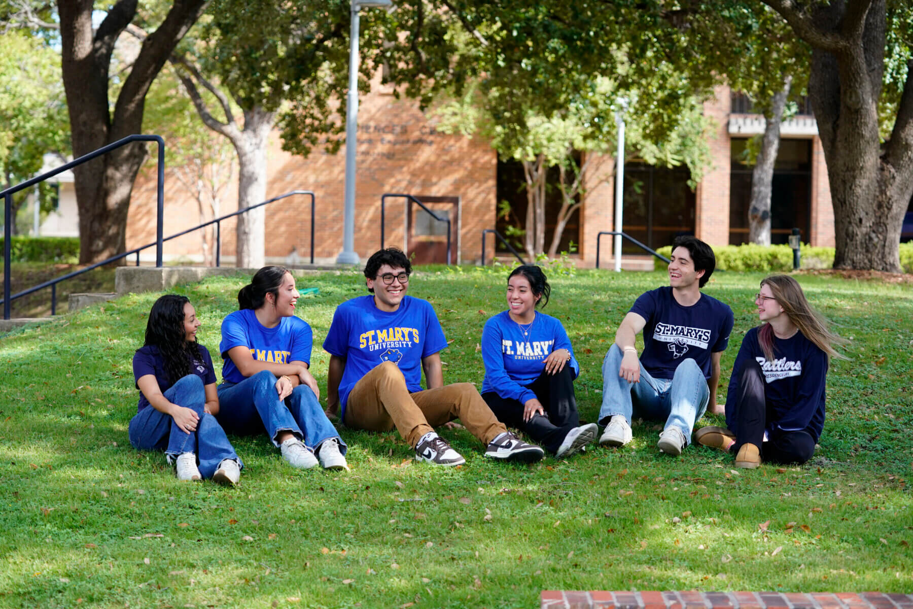 A group of students wearing St. Mary's University shirts sit on the grass in the courtyard.