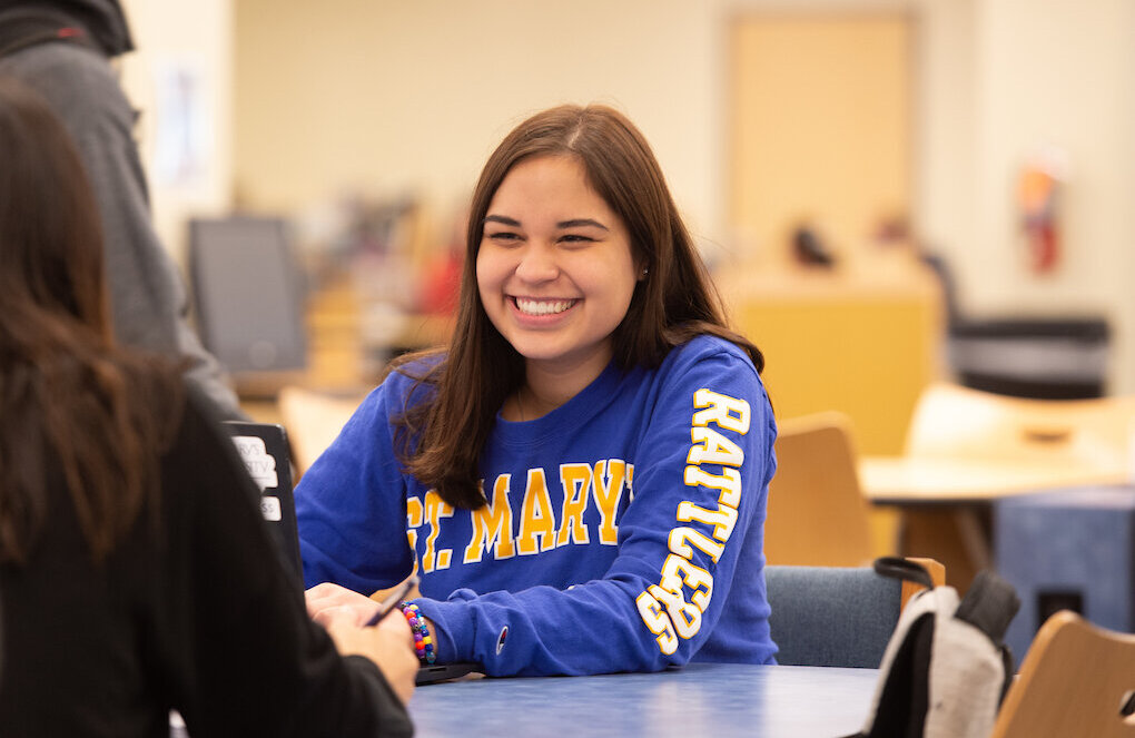 Female student wearing a St. Mary's University shirt smiles at her friend.