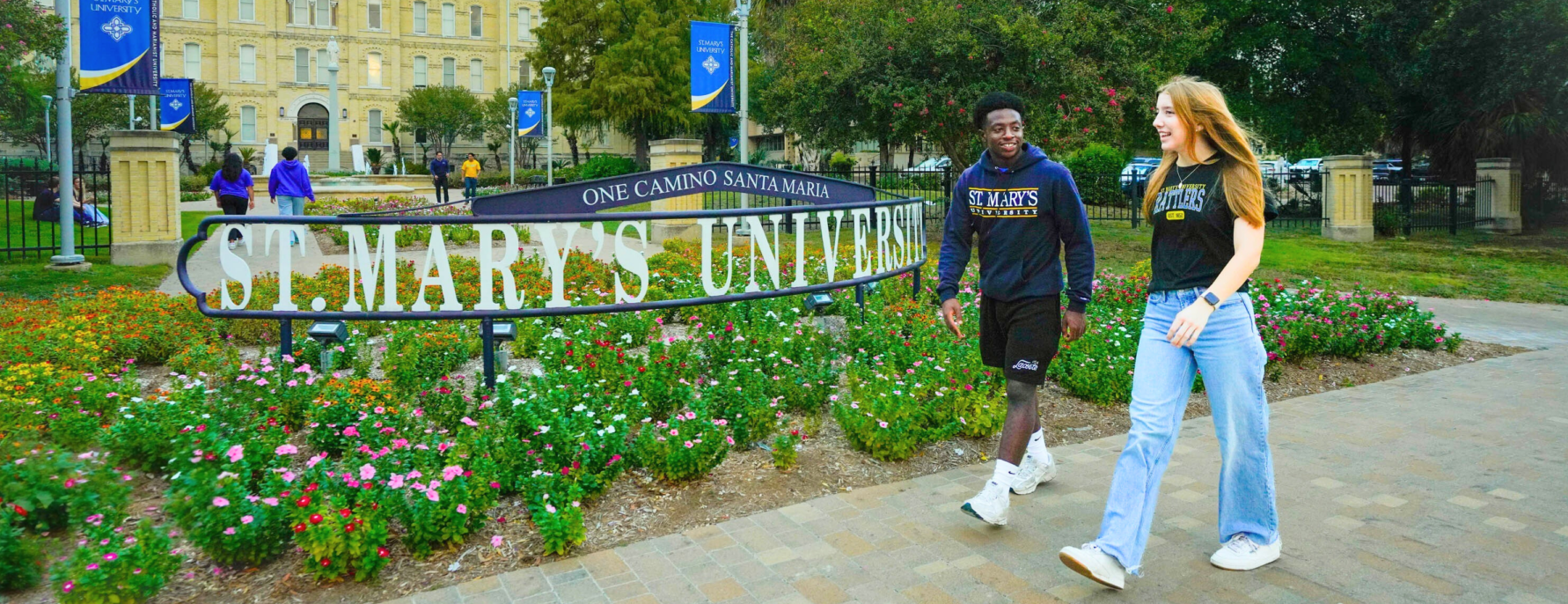Two students walking past the St. Mary's University sign in front of St. Louis Hall.