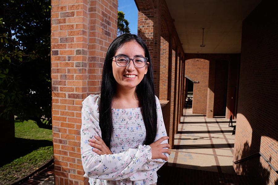 A student smiles with arms crossed at the top of brick-covered stairs.