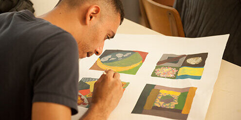 Student painting four different designs on whit poster board.