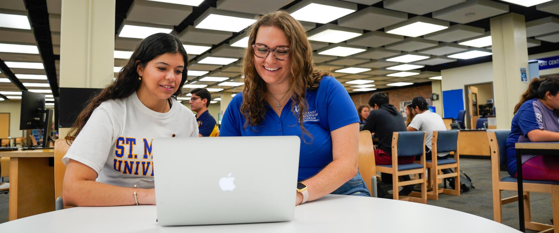 Two females sitting at a table with a laptop in the library. 