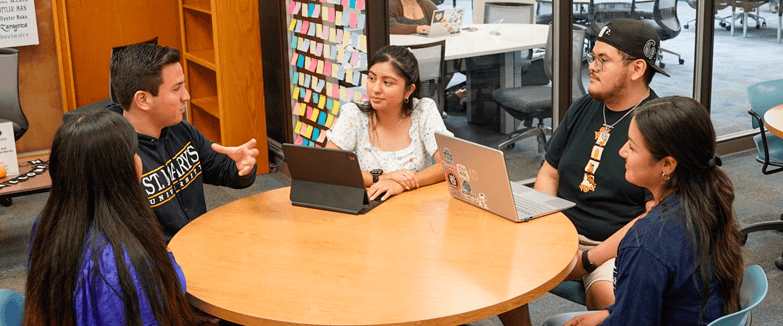 A group of students sitting at a table in the library Graduate Center for Excellence.