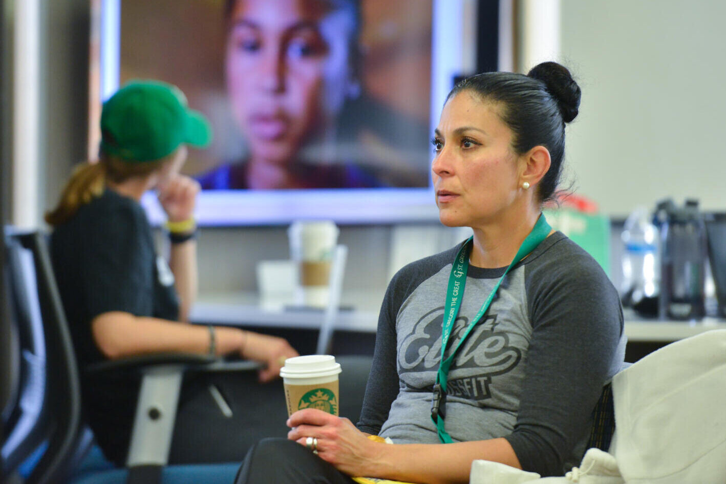 Female student holding a coffee cup while another student observes a video on the television.