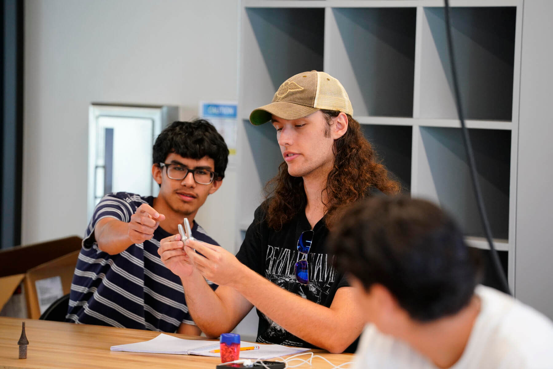 Students working together on a project. The student on the far side reaches over and helps another student adjust on of the pieces he is holding.