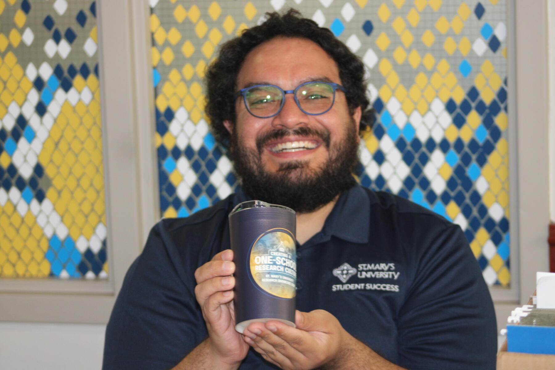 A male student happily holds up a thermos with the St. Mary's University Research Showcase logo on it.