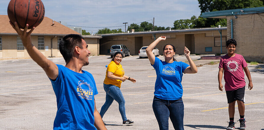 Male student wearing a St. Mary's blue shirt, holds a basketball about to be thrown to three students.