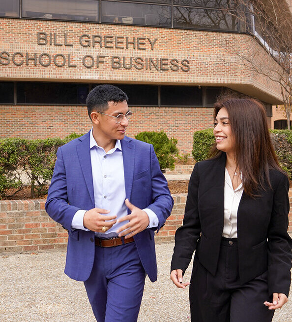 Two students walking outside by the Bill Greehey School of Business building.