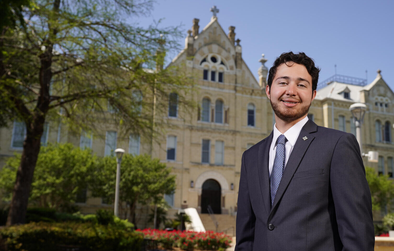 Male student wearing a suit stands in front of St. Louis Hall and smiles.