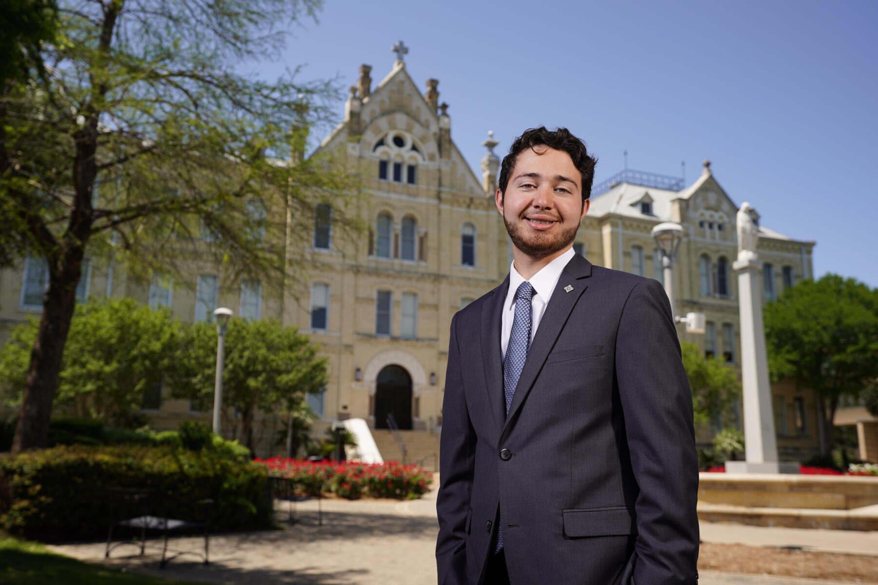 Male student wearing a suit stands in front of St. Louis Hall and smiles.