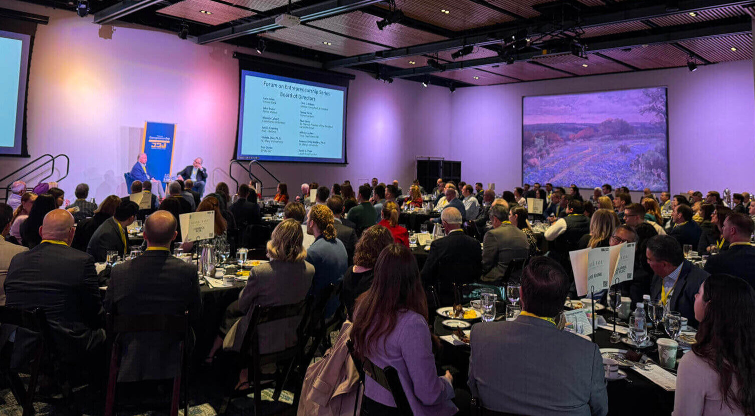 Group of people sitting at many tables in a conference room.