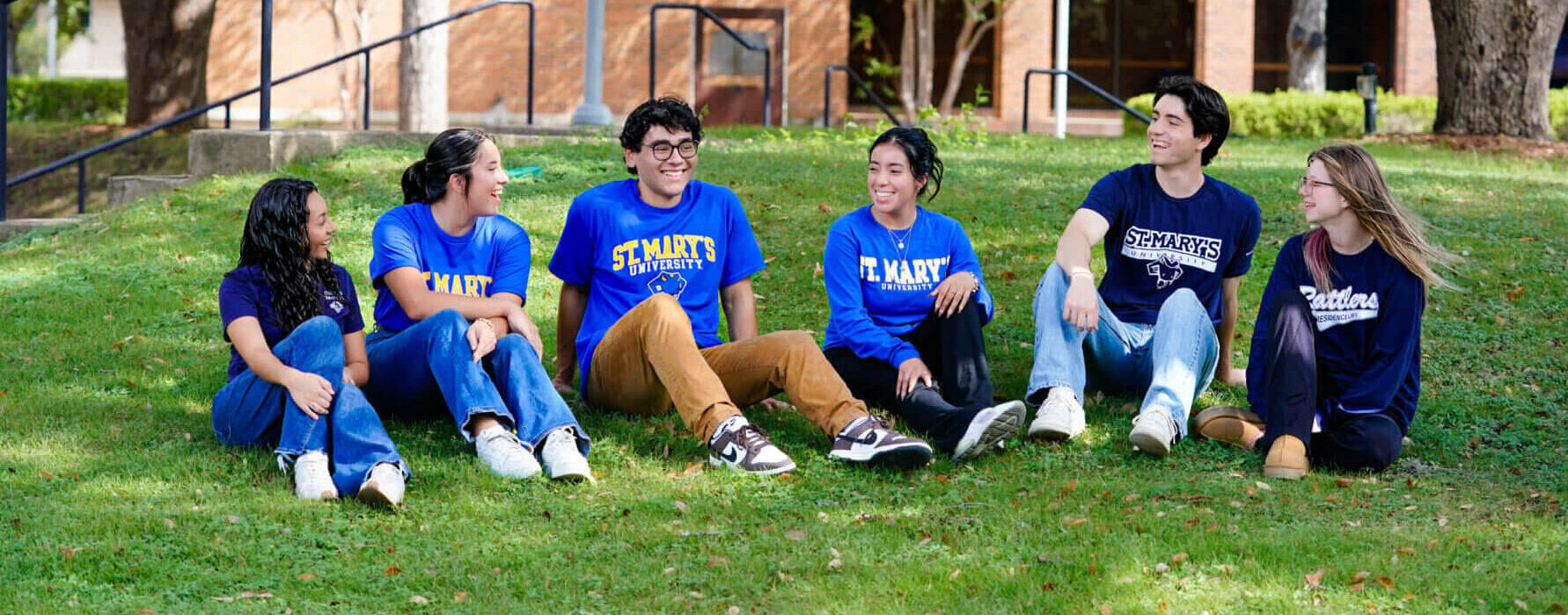 A group of students sit on a grassy hill on the St. Mary's University campus.